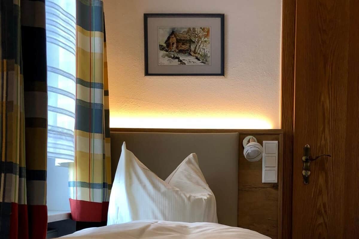 Ein Hotelzimmer mit Bett, Kopfteil, einem gerahmten Bild an der Wand und einer Tür mit Griff.