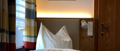 Una habitación de hotel con una cama, cabecera, un cuadro enmarcado en la pared y una puerta con manija.