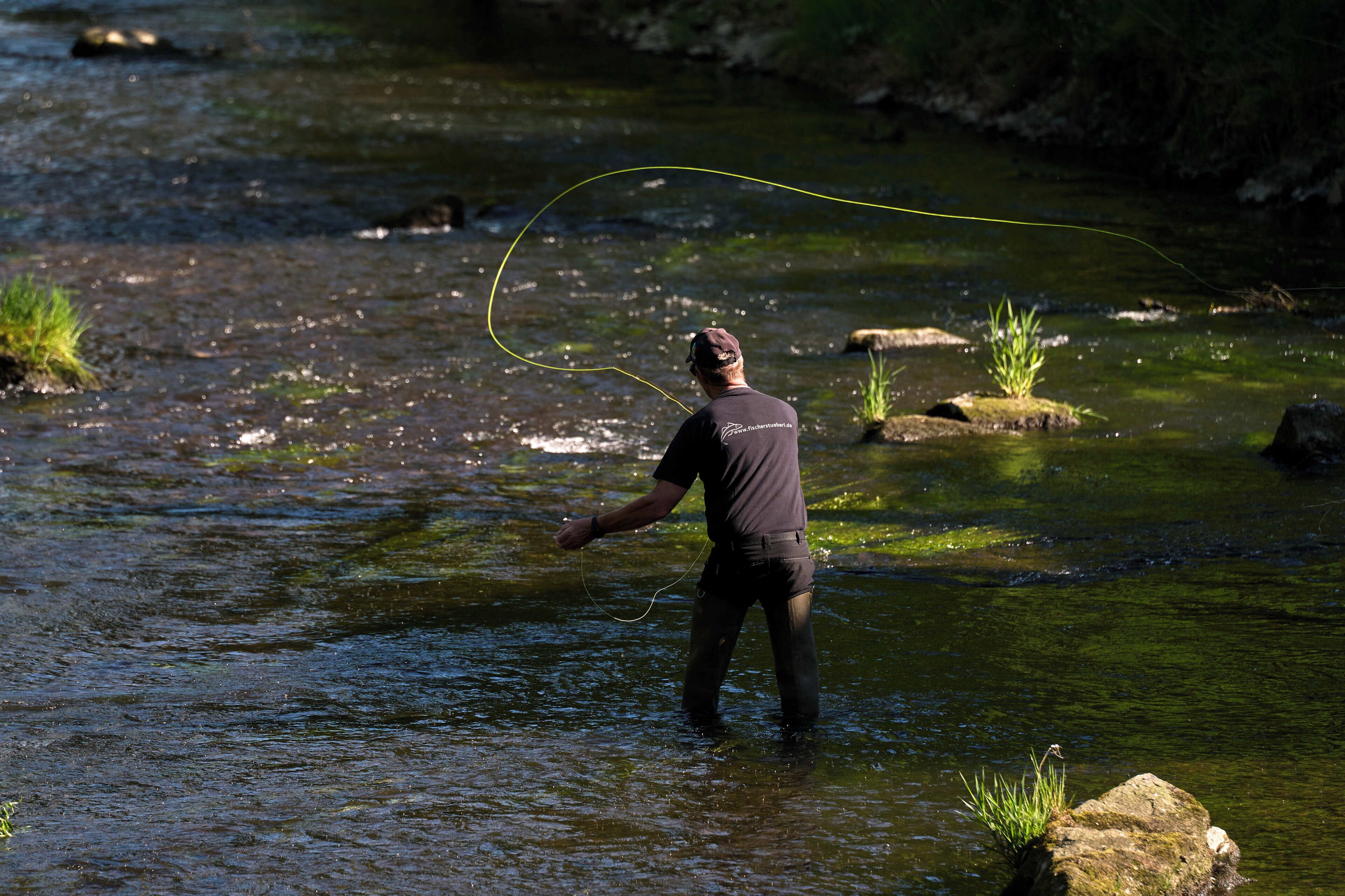 Una persona de pie en un río con una caña de pescar.