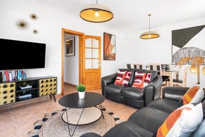 Un salon avec un canapé en cuir noir, une table basse ronde, un téléviseur fixé au mur et une bibliothèque.
