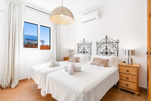 Habitación de hotel con dos camas, un ventanal grande, una lámpara colgante, una mesita de noche de madera y un aire acondicionado instalado en la pared.