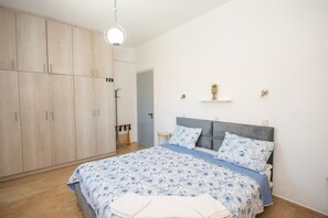 A bedroom with a bed, a wardrobe, a bedside table, and a wall-mounted shelf with a plant.