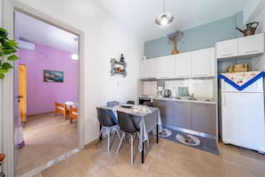 A compact kitchen with white cabinets, a dining table with chairs, and a small refrigerator.