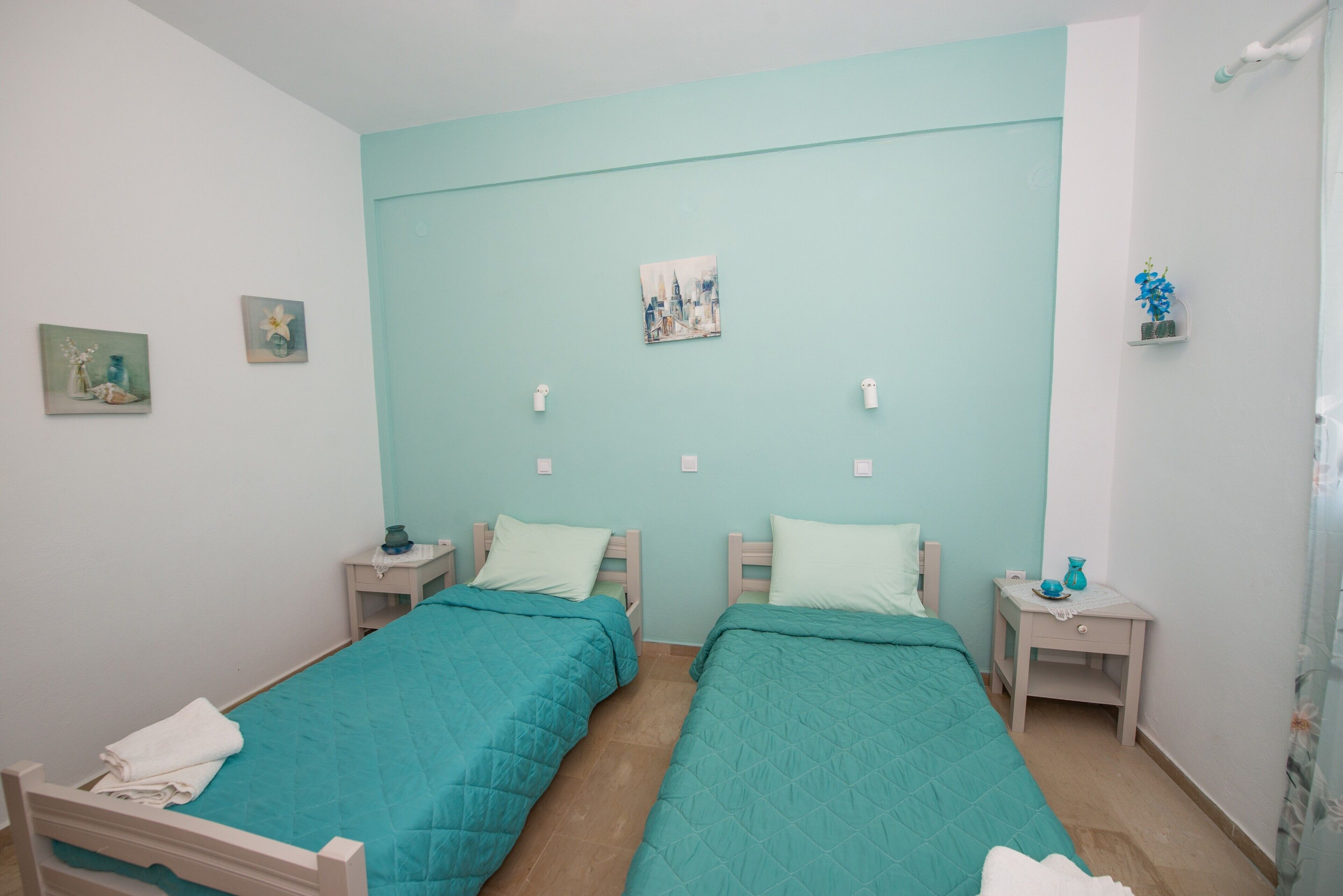 Camera matrimoniale con due letti, un piccolo comodino con lampada, un quadro appeso al muro e una piccola mensola con un vaso.
