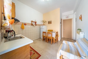 A compact kitchen with a sink, wooden cabinets, a tiled backsplash, and a dining area with a table and chairs.