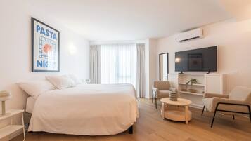 A modern hotel room with a large bed, a TV mounted on the wall, a small round table, and a chair.