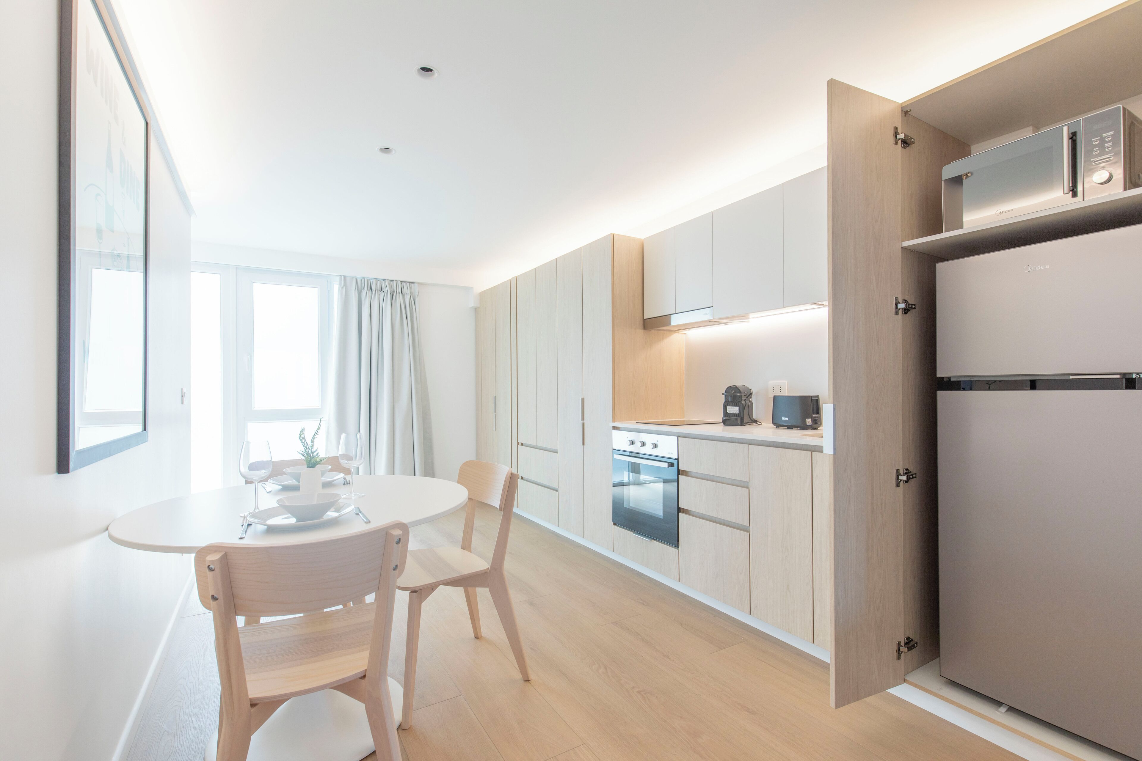 Een moderne keuken met een inbouwoven, een koelkast en een eethoek met een tafel en stoelen.
