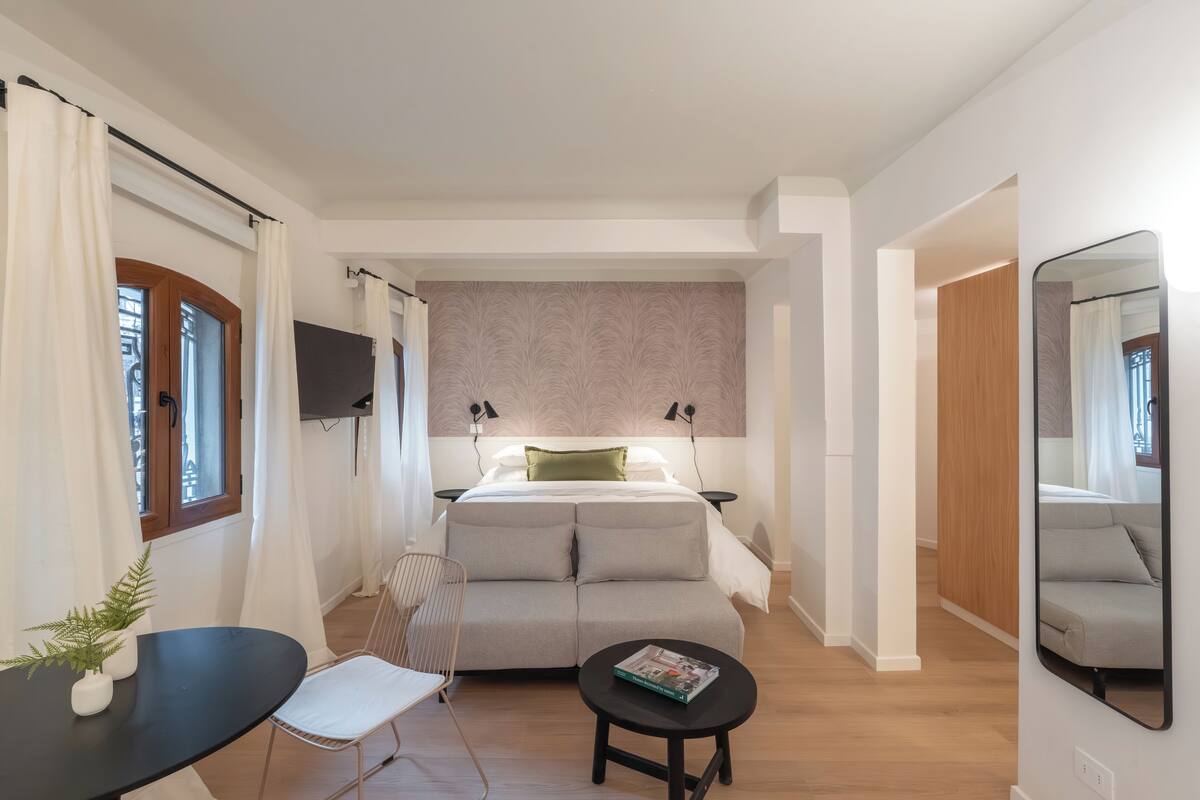 A modern bedroom with a bed, bedside tables, a small table with a magazine, a chair, and a mirror.