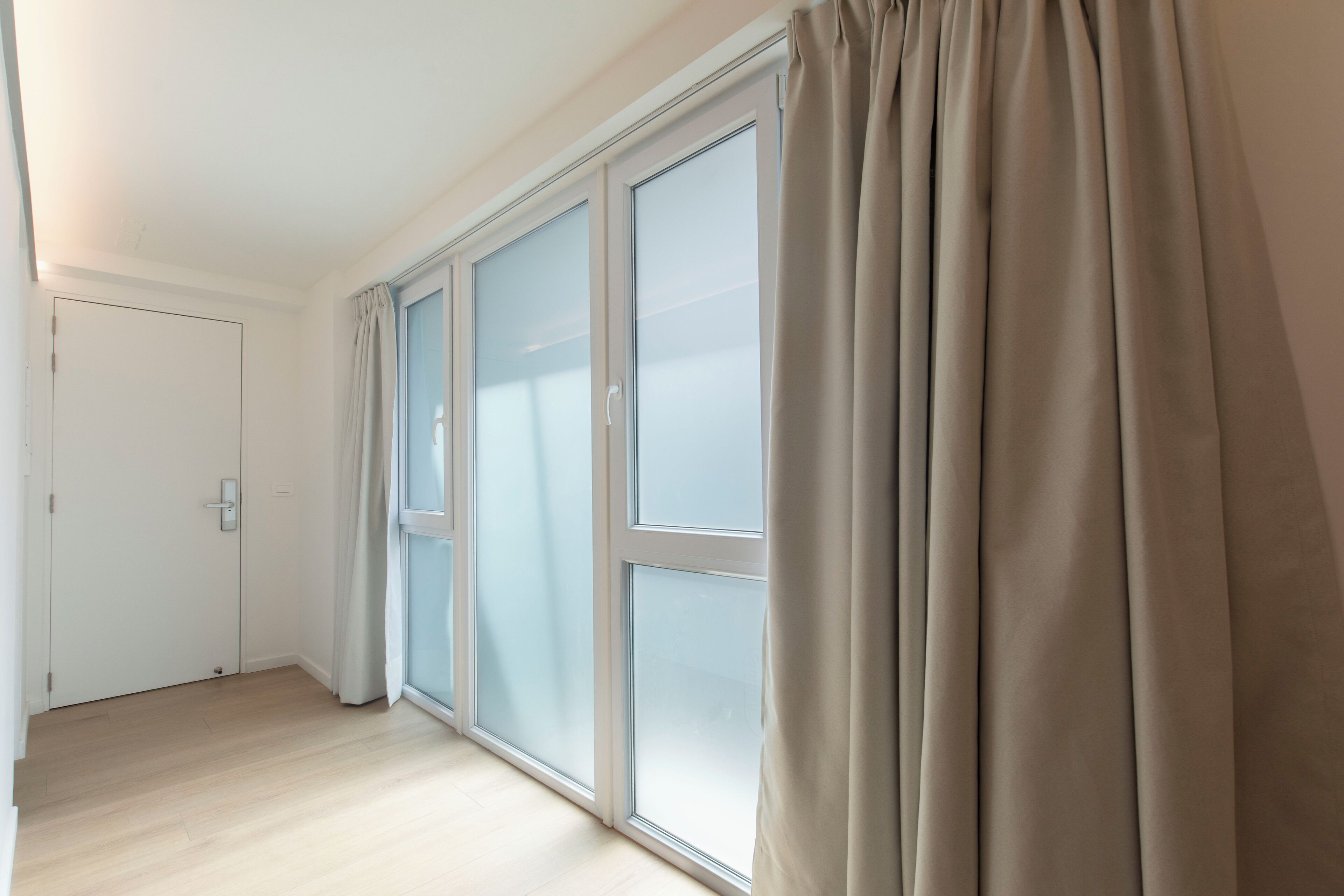 A room with a sliding glass door, a white door, and a light-colored floor.