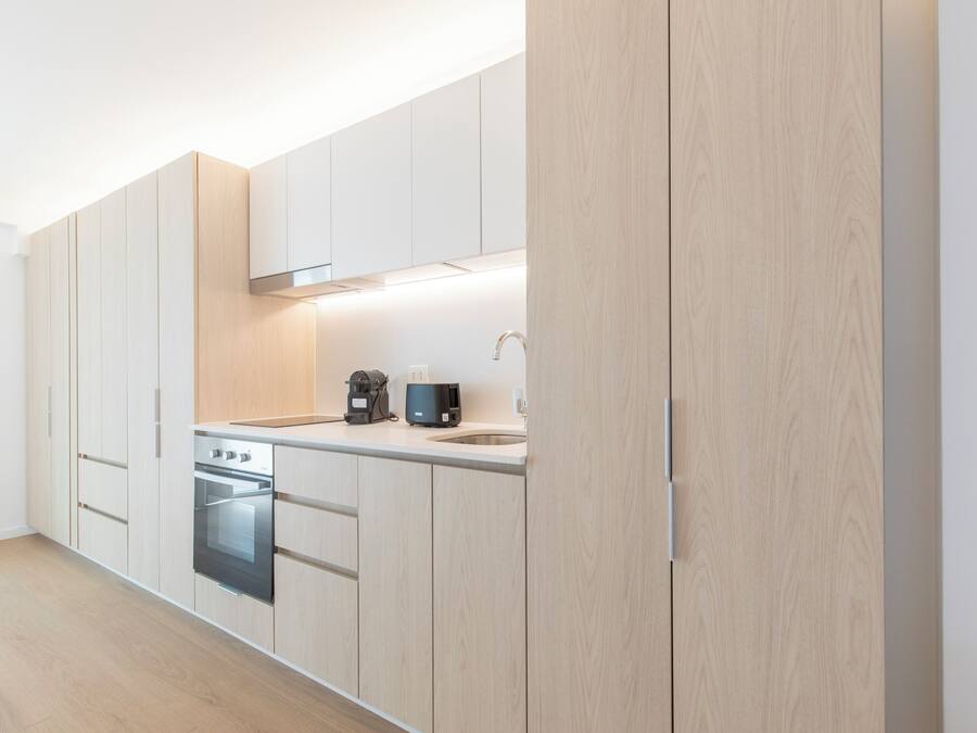 A modern kitchen with light wood cabinetry, a built-in oven, and a coffee maker on the countertop.