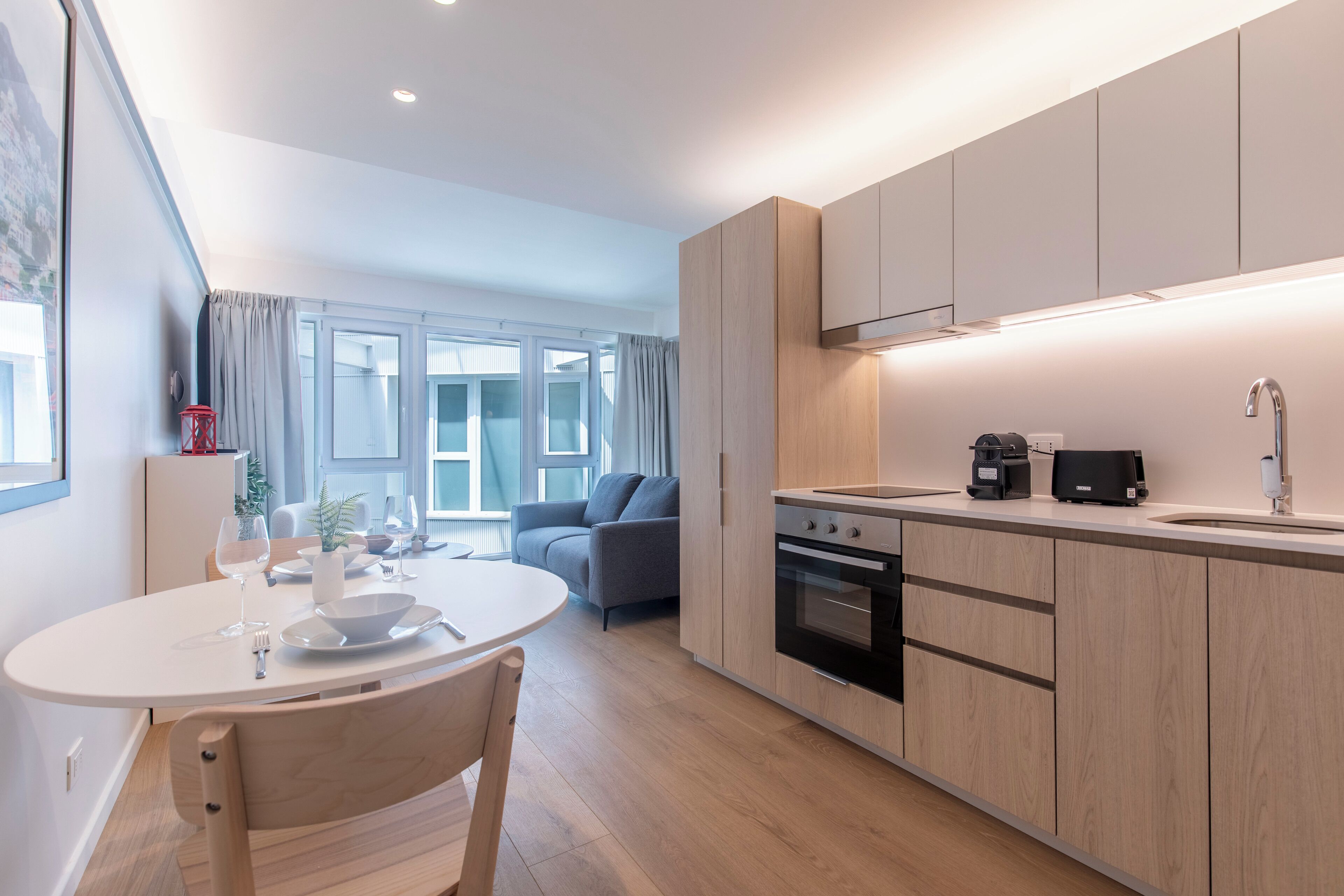 A modern kitchen with wooden cabinets, a dining table with chairs, and a built-in oven.