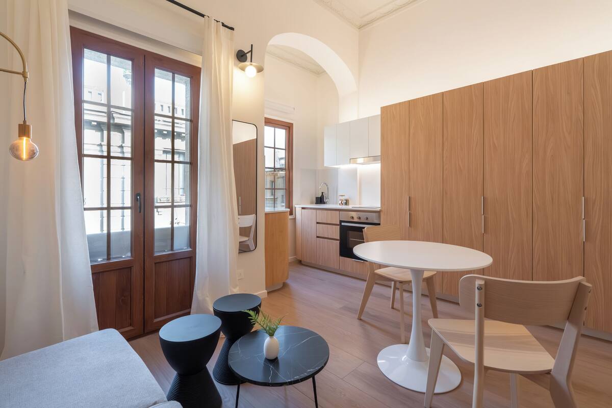 A modern kitchen with wooden cabinets, a dining area with a round table and chairs, and a small side table with a plant.
