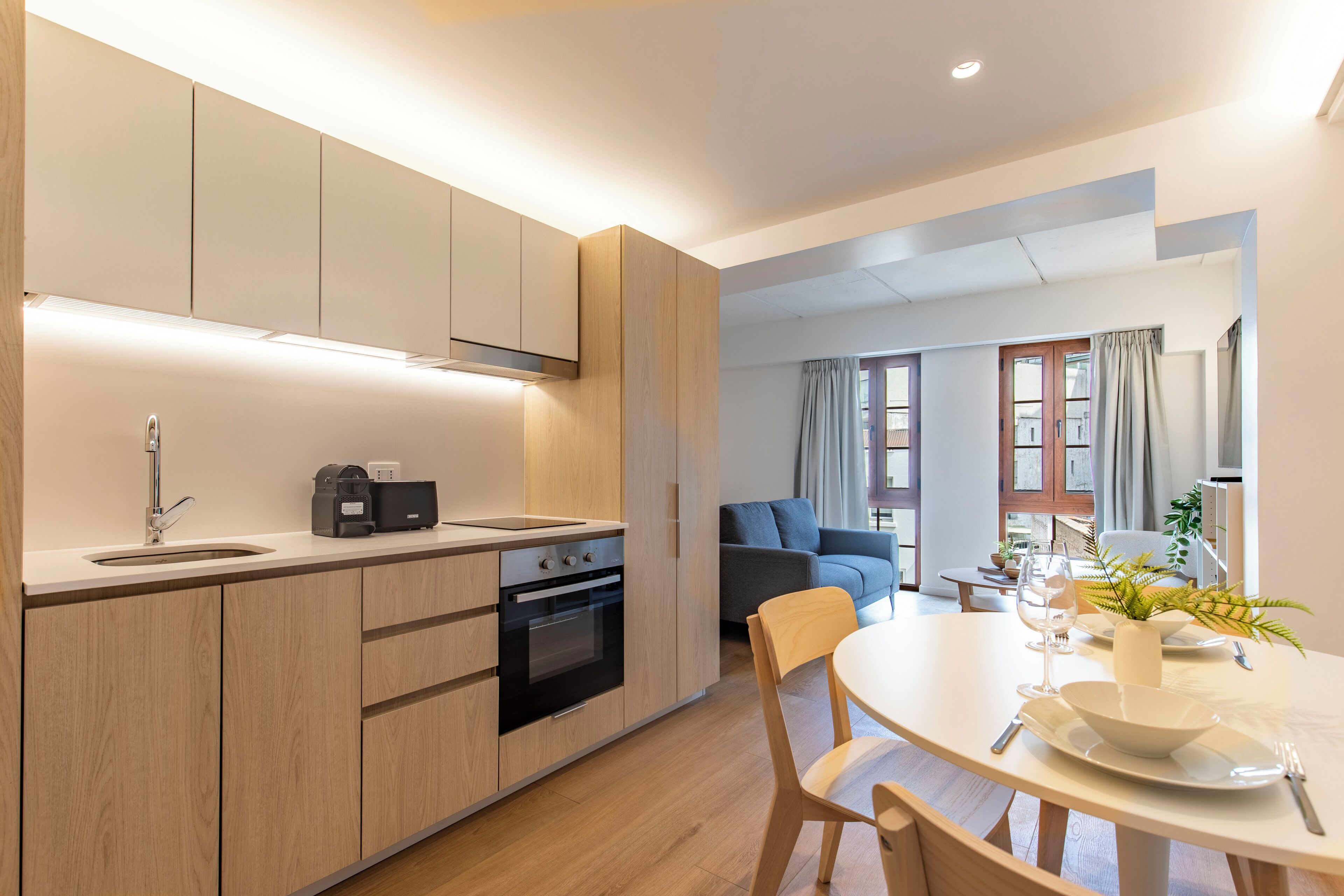 Una cocina moderna con armarios de madera, horno integrado y comedor con mesa y sillas redondas.