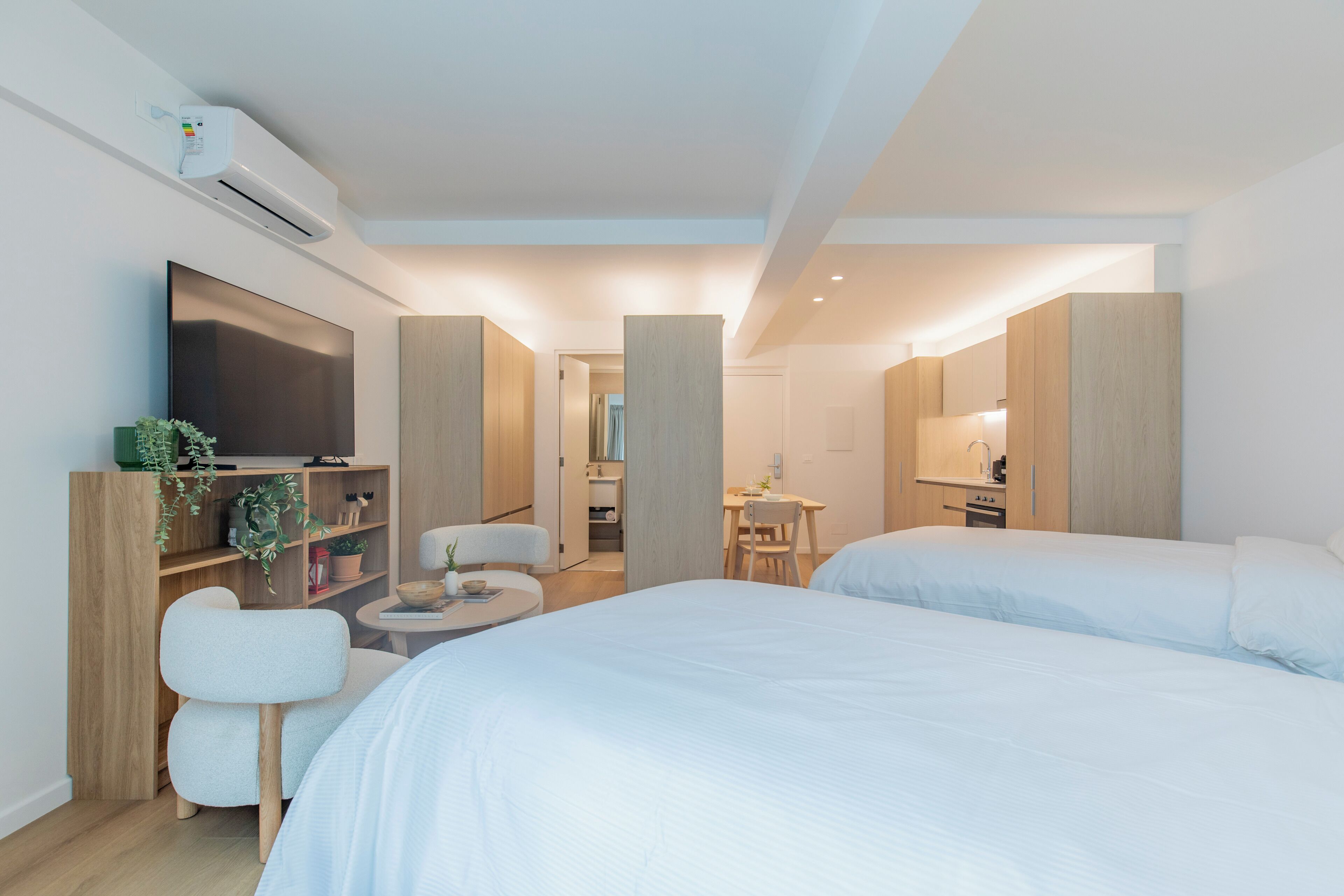 A modern hotel room with two beds, a TV, a desk, and a bathroom visible through an open door.