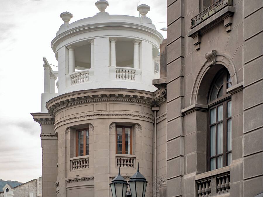 Un edificio histórico con una torre redonda, ventanas grandes y un balcón con barandilla.