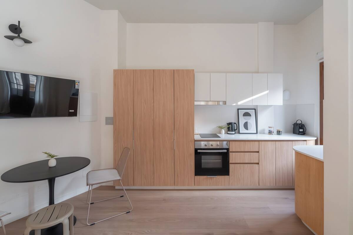 A modern kitchen with a built-in oven, a dining area with a table and chairs, and a TV mounted on the wall.