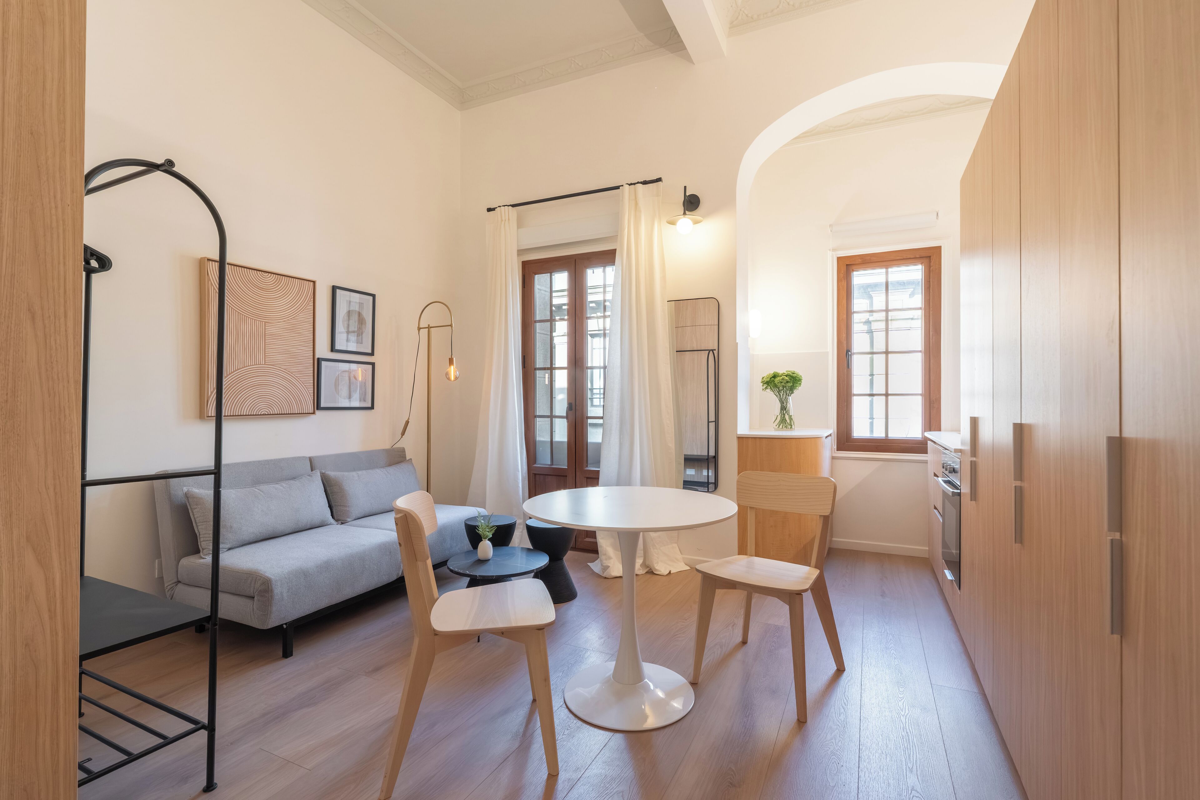Un espacio habitable compacto con un sofá, dos sillas, una mesita y una cocina con armarios de madera y un refrigerador.