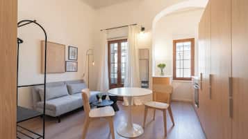 Un espacio habitable compacto con un sofá, dos sillas, una mesita y una cocina con armarios de madera y un refrigerador.
