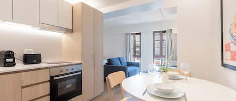 Una cocina moderna con electrodomésticos integrados, un comedor con una mesa redonda y sillas, y vistas de la ciudad a través de amplios ventanales.