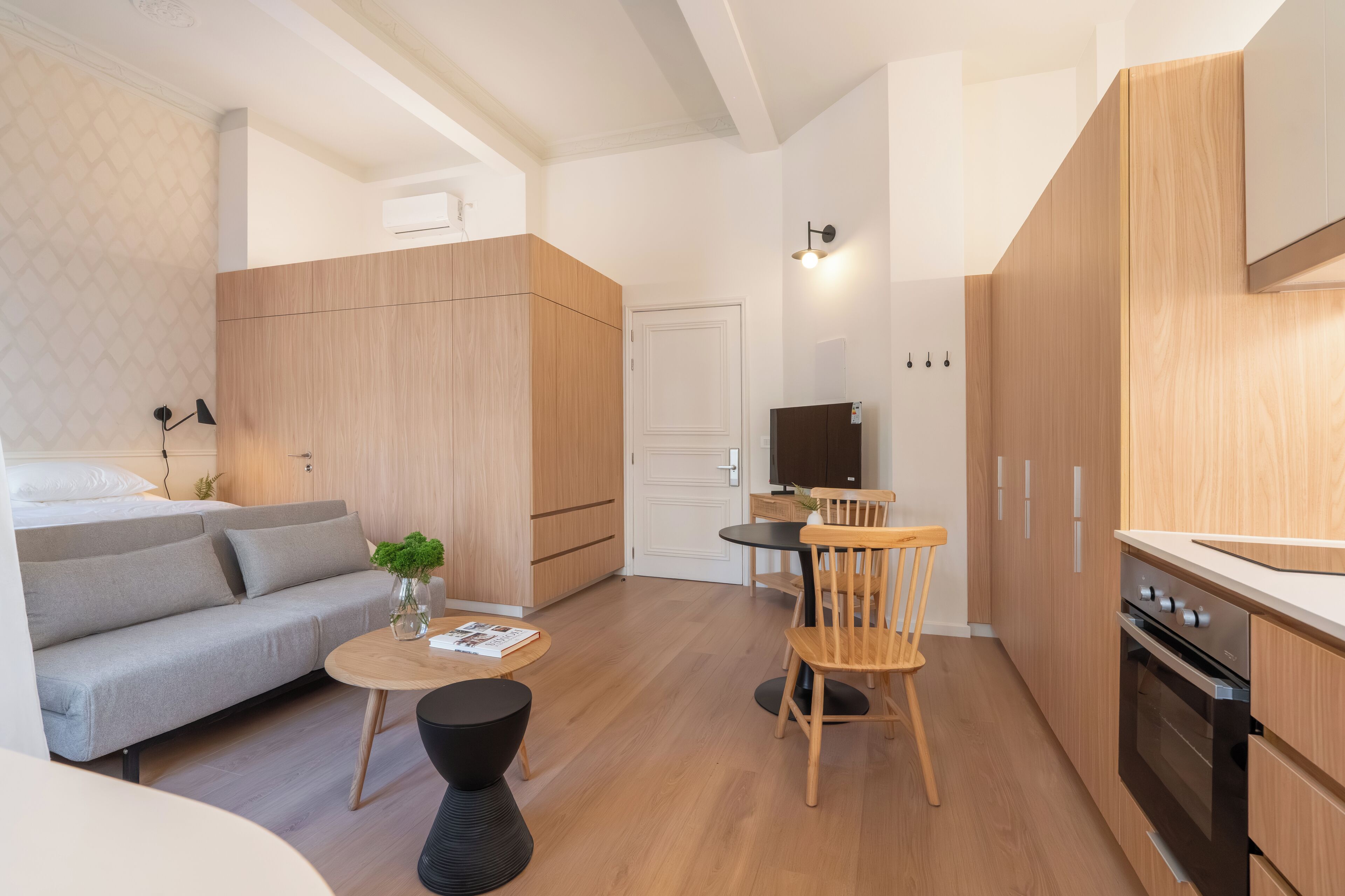 A modern, compact living space with a sofa, dining table, chairs, and a kitchenette.