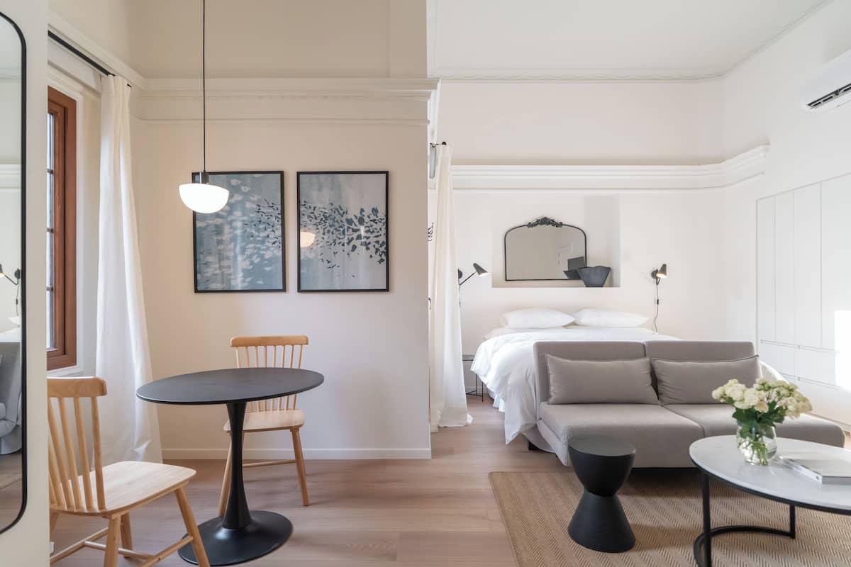 A modern hotel room with a bed, a sofa, a dining table with chairs, and artwork on the walls.