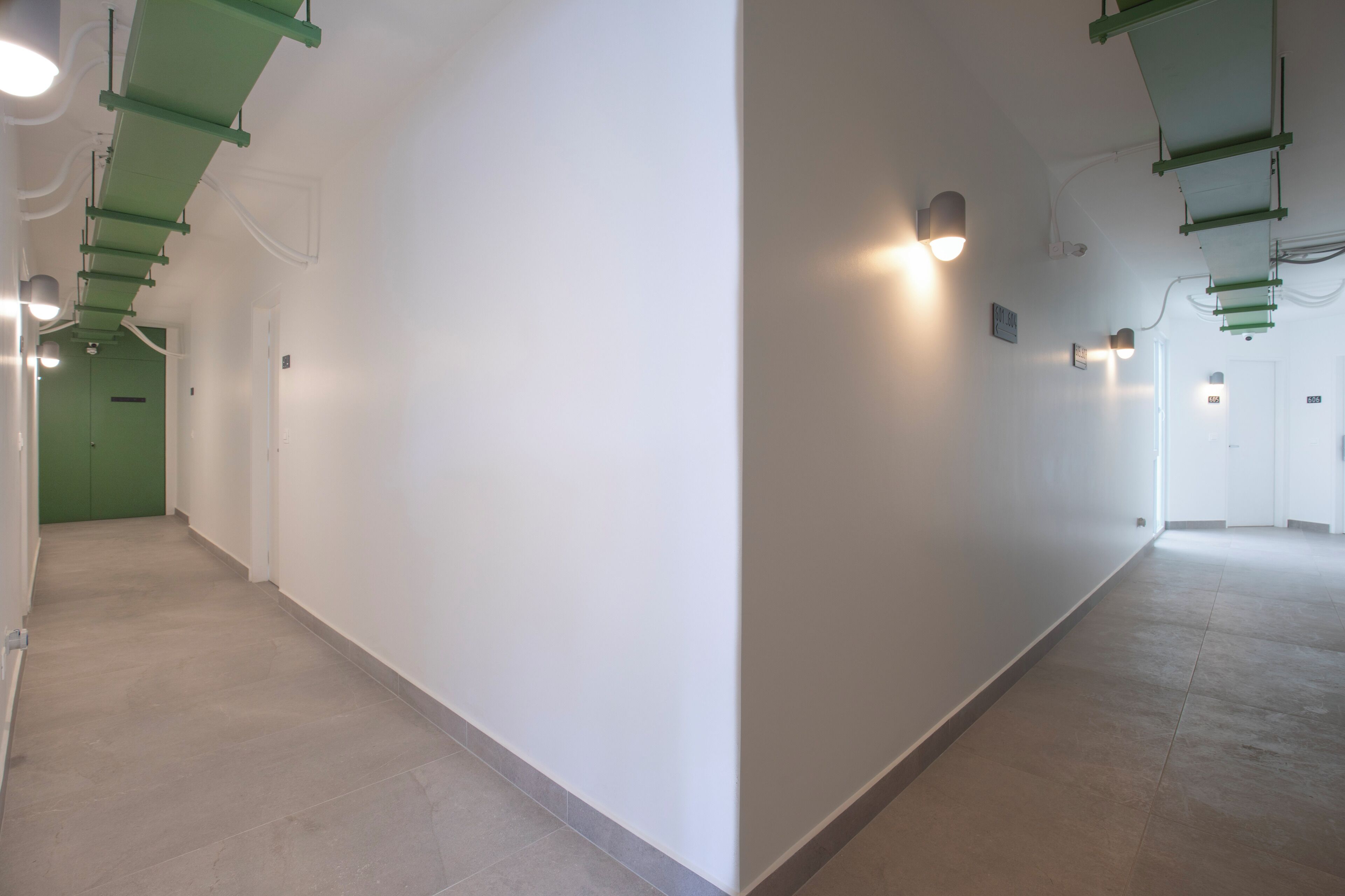 A long, narrow hallway with white walls and green structural elements.