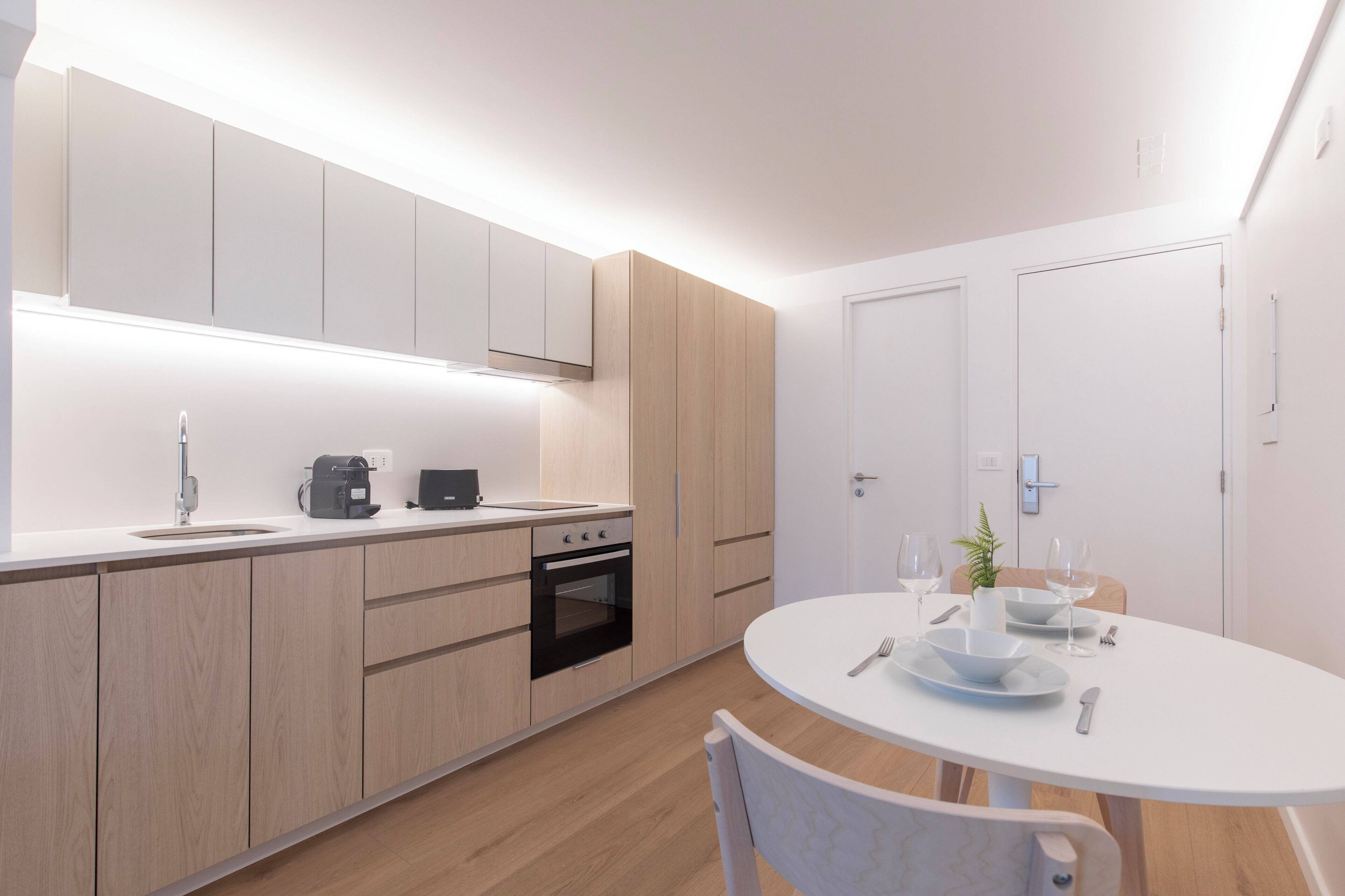 Una cocina moderna con armarios de madera, horno integrado y un comedor con mesa y sillas blancas.