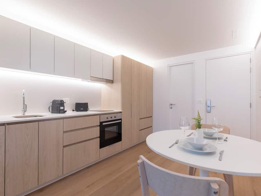 Una cocina moderna con armarios de madera, horno integrado y un comedor con mesa y sillas blancas.