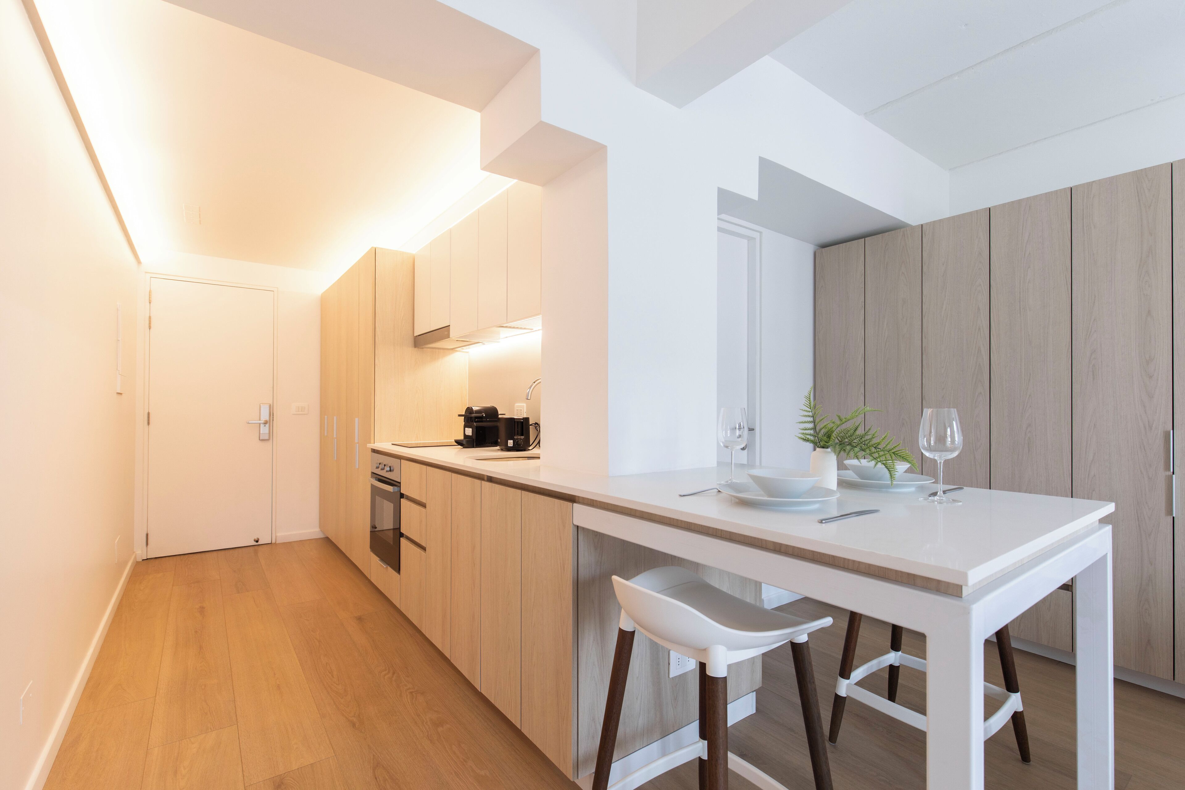A modern kitchen with a white countertop, wooden cabinets, and a bar stool.