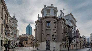 Un edificio histórico con arquitectura clásica, una calle adoquinada y un rascacielos moderno al fondo.