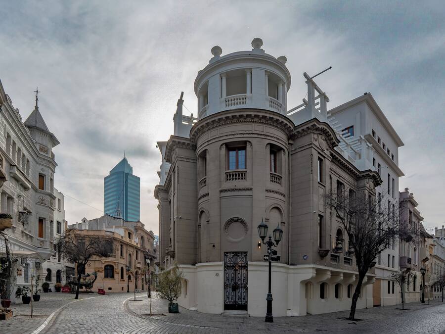 Un edificio histórico con arquitectura clásica, una calle adoquinada y un rascacielos moderno al fondo.