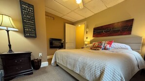 Habitació d'hotel amb un llit, un taulell, una làmpada, un quadre i una paret amb noms de ciutats.