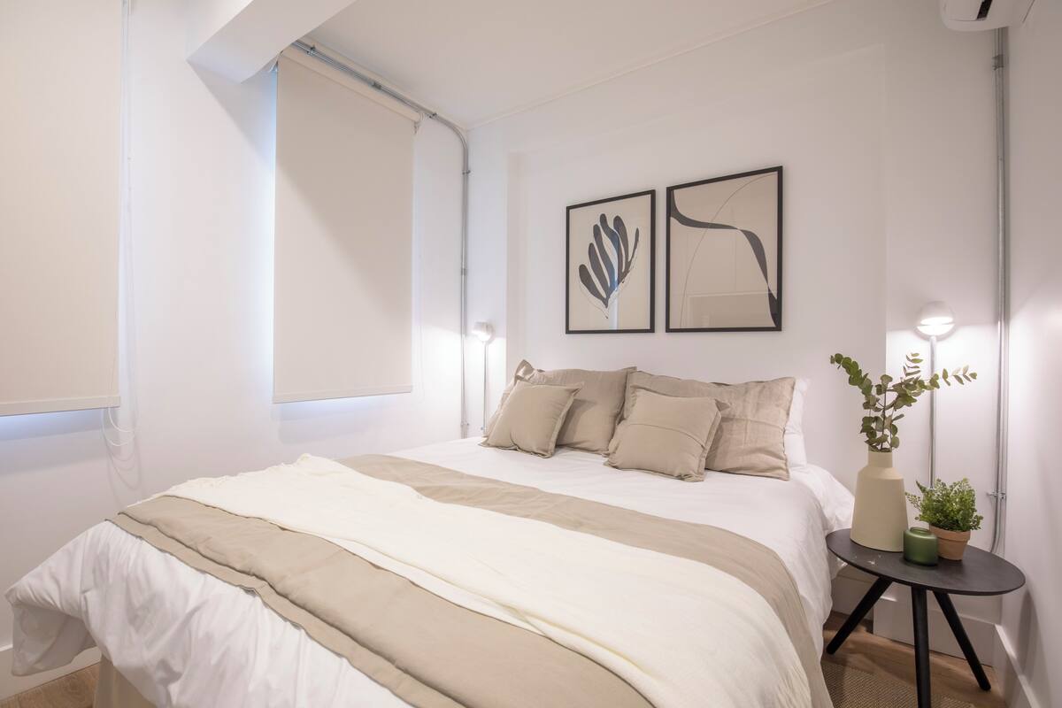 Un dormitorio moderno con una cama grande, una mesita de noche con lámpara y dos cuadros enmarcados en la pared.