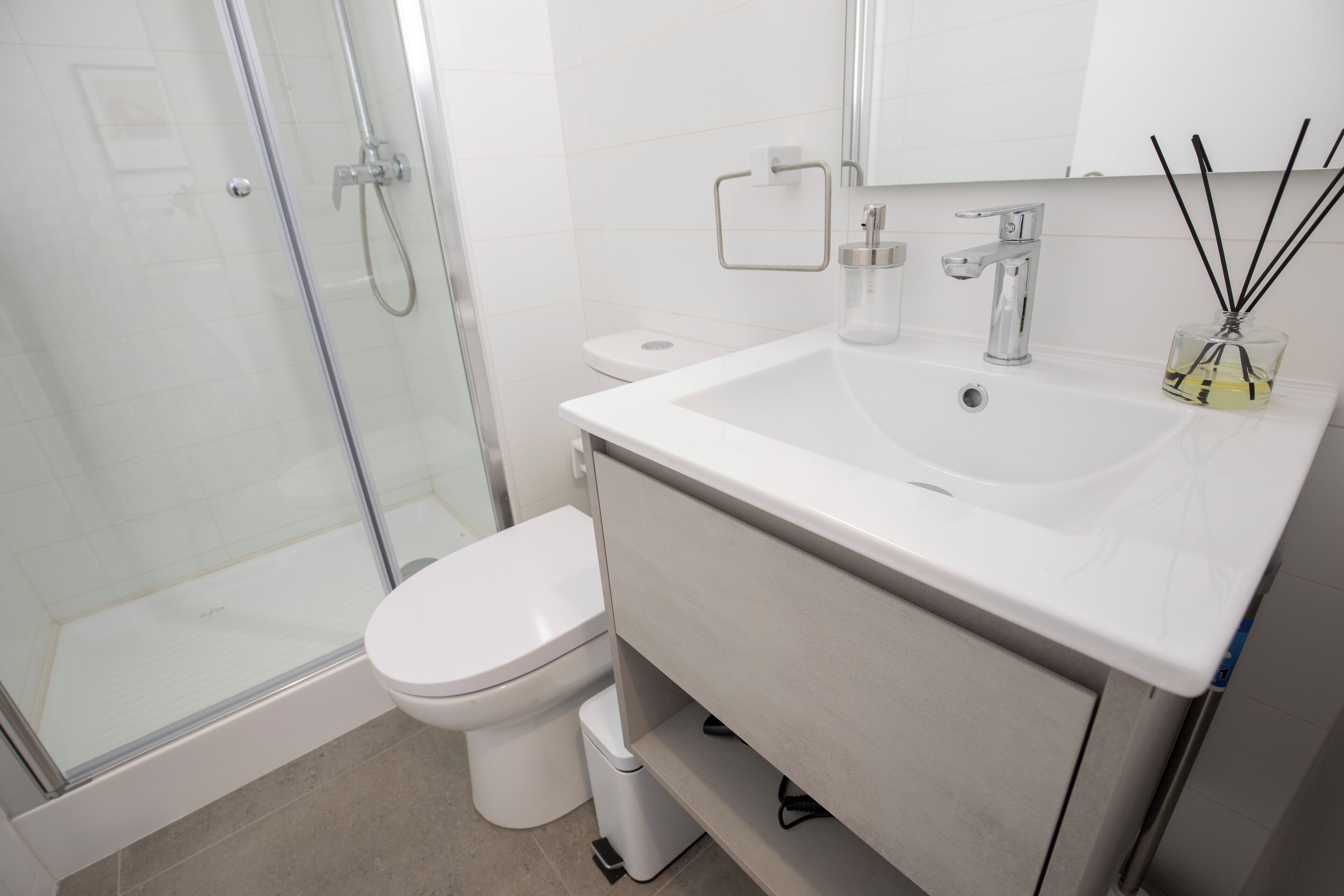 Un baño moderno con ducha envuelta en vidrio, un inodoro blanco y un lavabo con espejo superior.