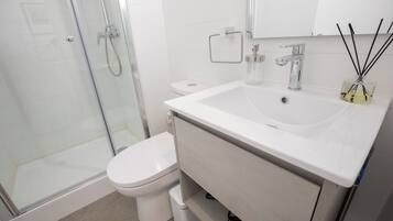 Un baño moderno con ducha envuelta en vidrio, un inodoro blanco y un lavabo con espejo superior.