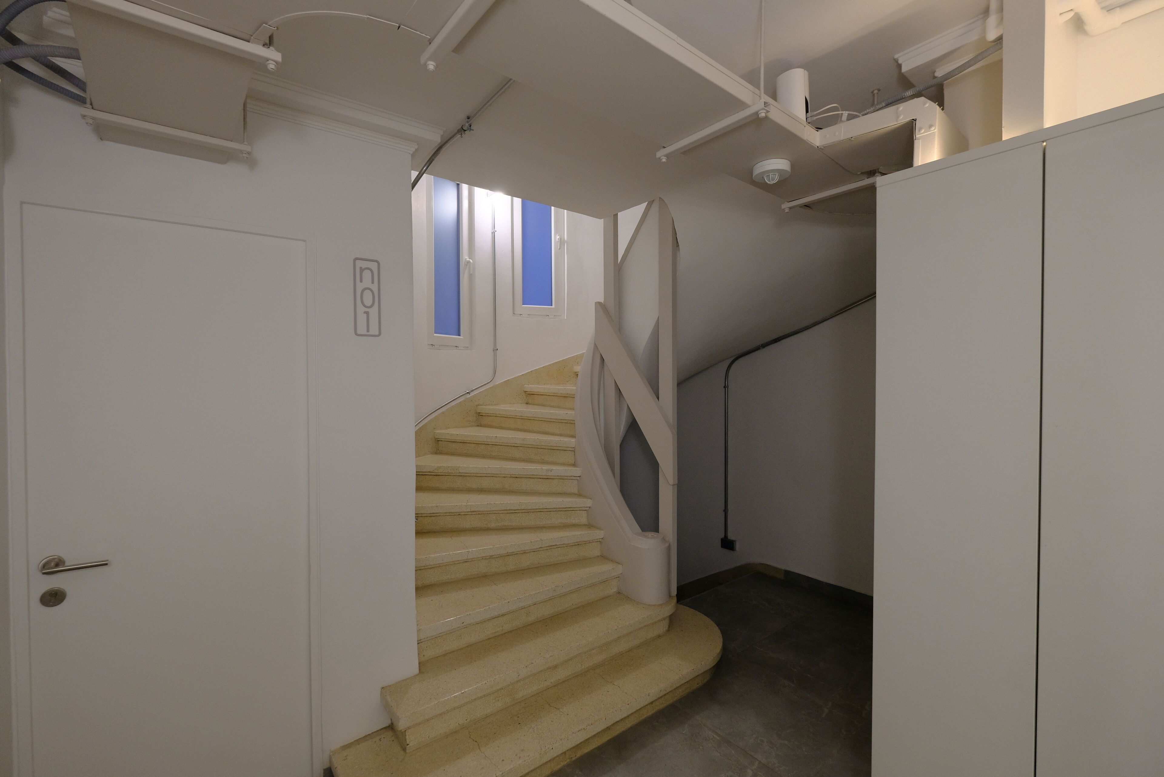 A staircase with a handrail, a door with a handle, and a window with blinds.