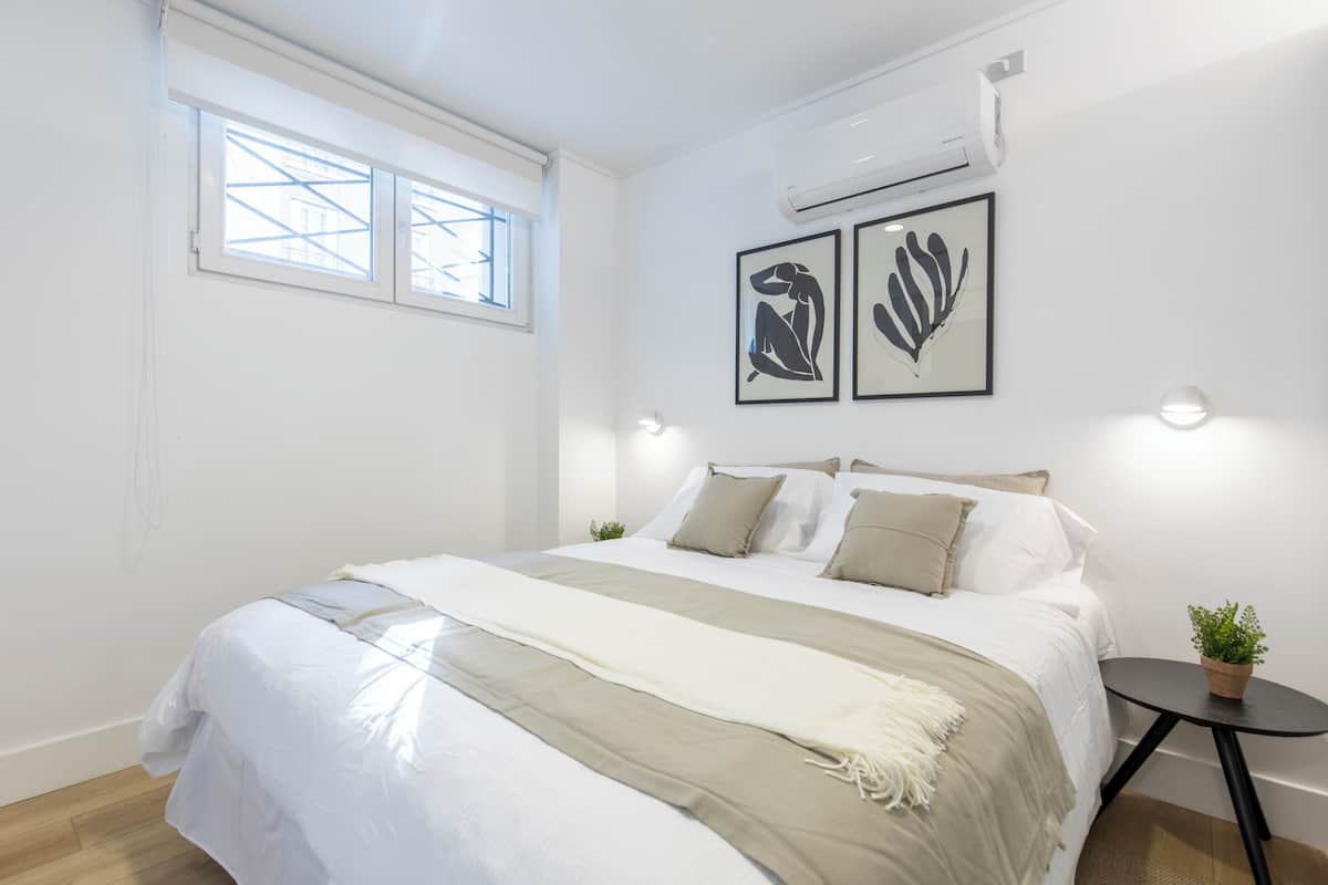 Un dormitorio con una cama, un ventanal y dos unidades de aire acondicionado instaladas en la pared.