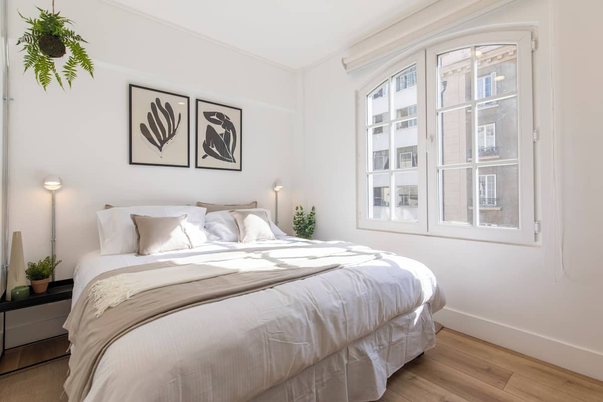 Un dormitorio con una cama grande, un ventanal y dos cuadros en la pared.
