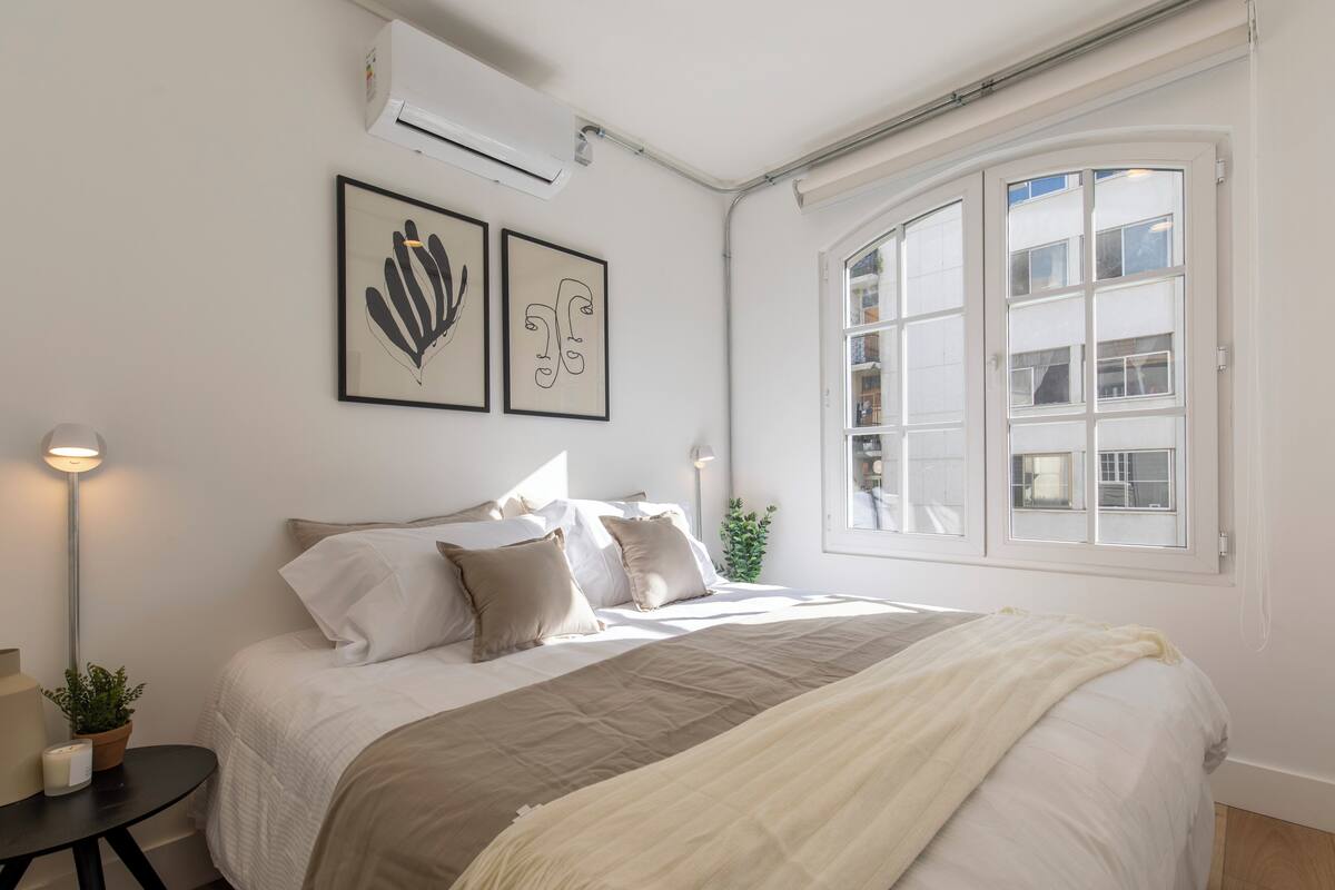 Un dormitorio con cama, mesita de noche, lámpara y un cuadro en la pared.
