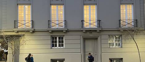 A building with multiple windows and balconies, a door with a glass panel, and a bench on the sidewalk.