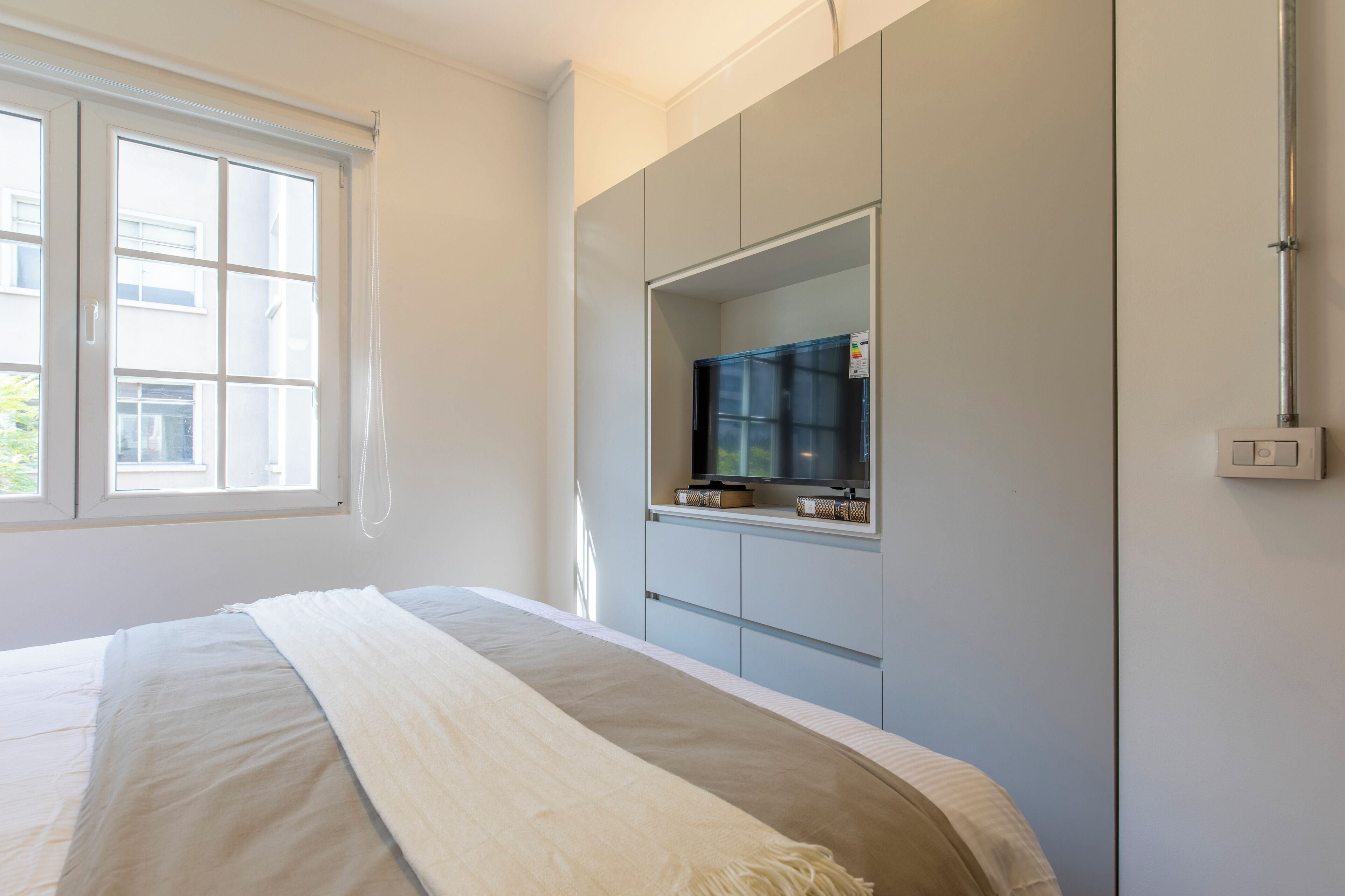 A bedroom with a bed, a large window, a wardrobe, and a television.