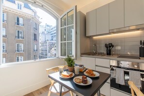A modern kitchen with a large window, a dining table with food, and a view of buildings outside. - Nest Bellas Artes (Santiago)