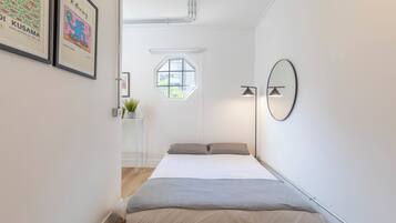 A bedroom with a bed, a window, a wall-mounted mirror, and framed artwork.
