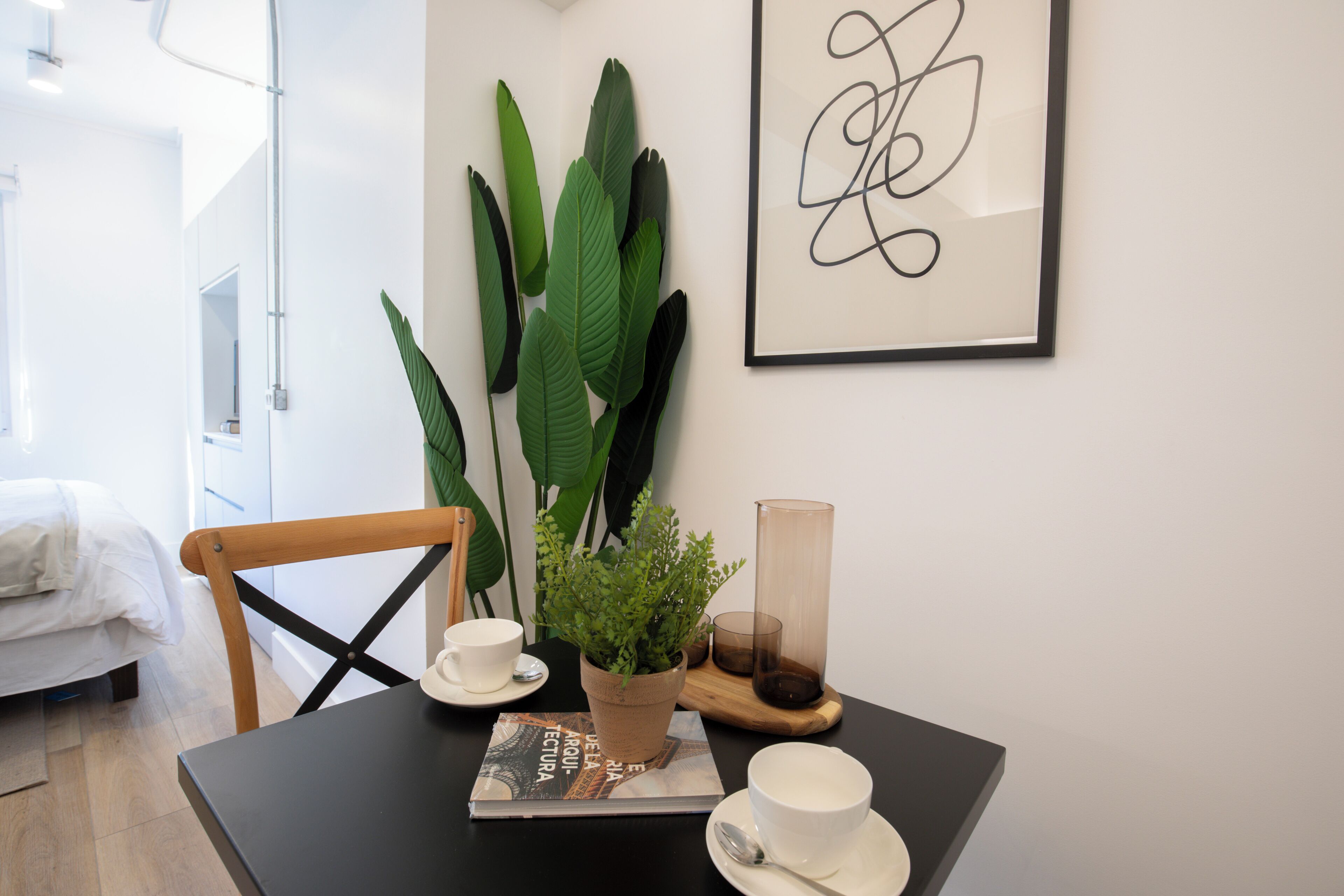A neatly arranged dining area with a table set for two, a potted plant, a framed artwork, and a candle holder.