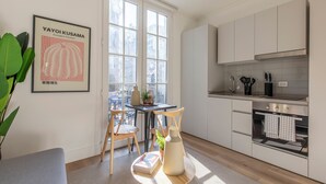 A modern kitchen with white cabinets, a dining area with a table and chairs, and a large window providing natural light. - Nest Bellas Artes (Santiago)
