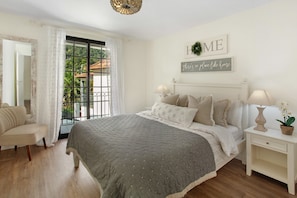 Un dormitorio con cama, mesitas de noche, una silla, una ventana con cortinas y adornos en la pared.