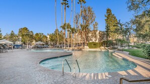 A swimming pool with a stone deck, surrounded by palm trees and lounge chairs. - Woodland Hill Condo with Pool, Gym, Free Parking (Los Angeles)