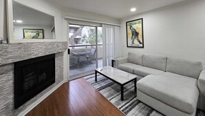 A modern living room with a fireplace, a sofa, a coffee table, and a poster on the wall. - Woodland Hill Condo with Pool, Gym, Free Parking (Los Angeles)