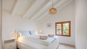 Un dormitorio con cama, mesita de noche, lámpara, ventana y vigas en el techo.