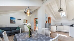 Una cocina moderna con armarios blancos, un comedor con mesa para cuatro, y una sala de estar con sofá y un cuadro.